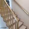 Detal złotej balustrady stalowej z prostym pochwytem przy schodach wykończonych panelami drewnopodobnymi Detal złotej balustrady stalowej z prostym pochwytem przy schodach wykończonych panelami drewnopodobnymi